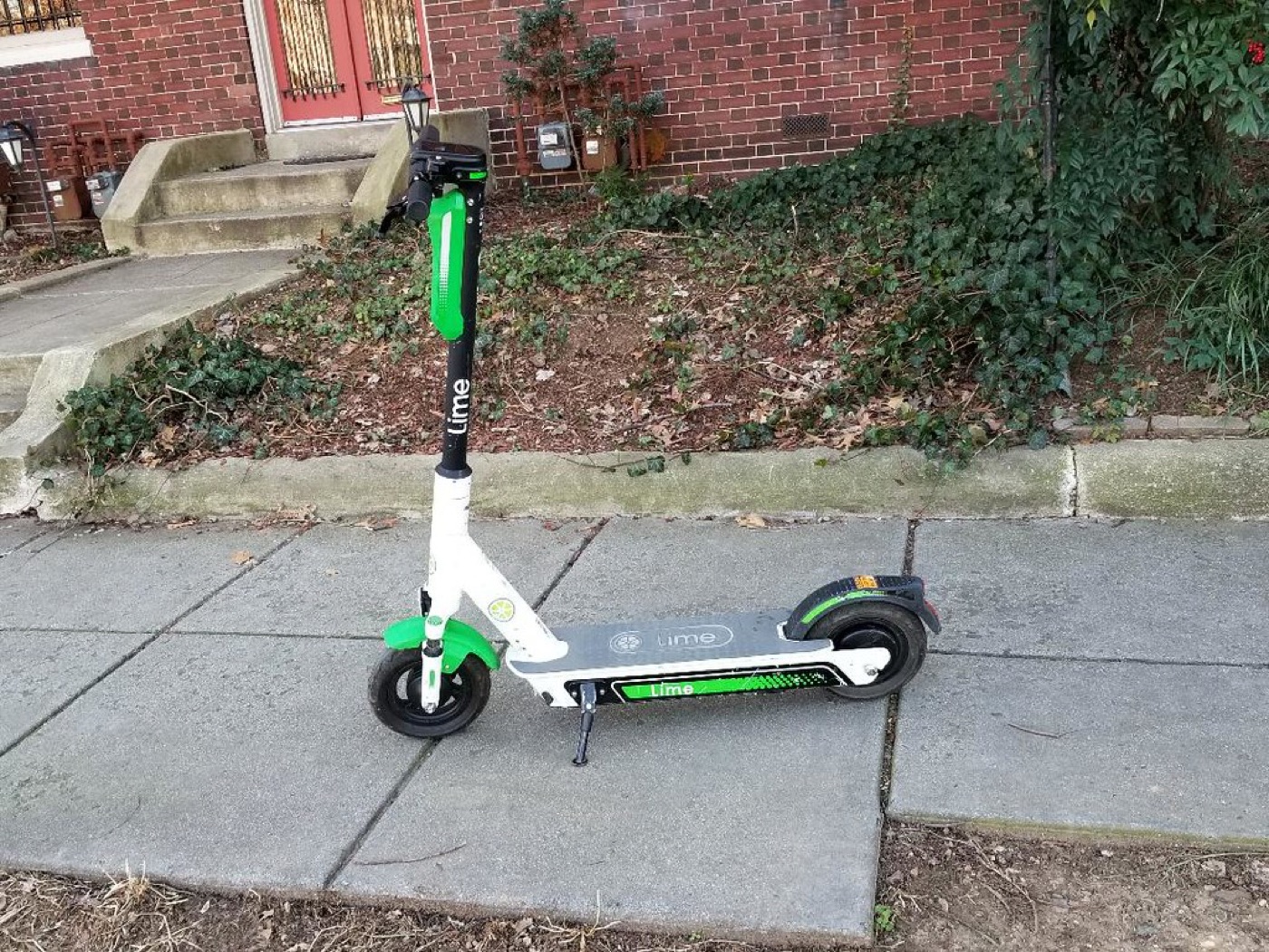 Shared scooter parked upright at the sidewalk edge with a clear pedestrian path.